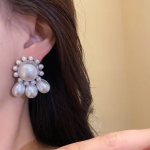 Detailed shot of vintage palace style pearl earrings with teardrop pendants on an ear.