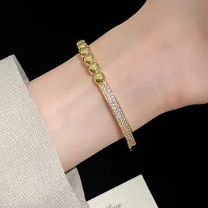 Gros plan détaillé d'un jonc plaqué or 18K avec zircons et perles au poignet.