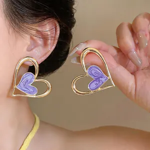 Detalle de pendientes de corazón de esmalte morado con borde dorado puestos.
