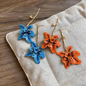 Detailed view of handmade tropical orchid floral earrings in blue and orange enamel