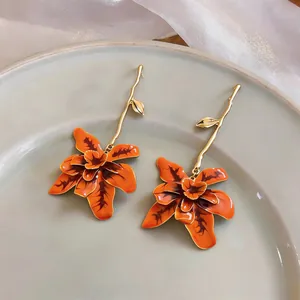 Close-up detail of artistic long orange floral drop earrings with gold branch stems design