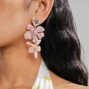 Primo piano di orecchini a fiore in resina rosa con perni a cuore e accenti di cristallo