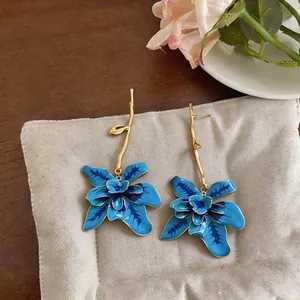Detailed macro view of blue floral drop earrings with elegant gold stems on a soft pad.
