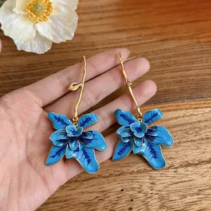 Macro detail shot of exaggerated blue enamel flower earrings with gold stems on hand