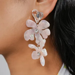 Primo piano di orecchini pendenti a fiore in resina rosa con strass indossati