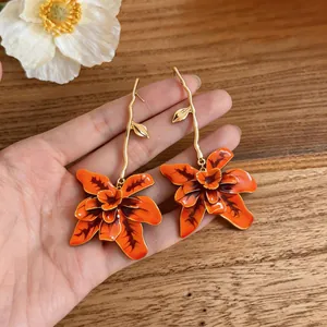 Close-up of orange floral dangle earrings with gold branch stud detail.