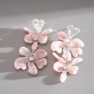 Dettaglio di orecchini a fiore in resina rosa marmorizzata con cuori e piccoli cristalli.