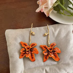 Detail of long orange flower dangle earrings with gold wavy stems on linen pad.