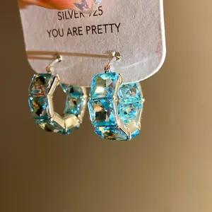 Dettaglio macro di orecchini a cerchio vintage in zirconi blu chiaro su carta bianca