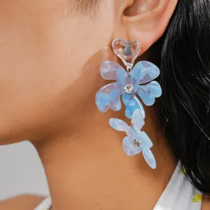Dettaglio di orecchini a fiore in resina blu con perni a cuore e strass su un modello