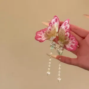Vue détaillée des boucles d'oreilles papillon brodées roses avec de longues perles.