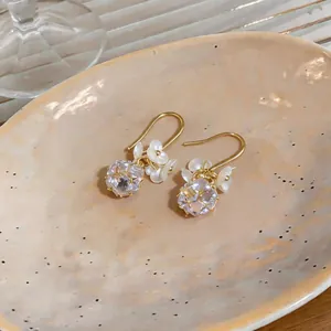 Detailed macro shot of French style gold hook earrings featuring zircon stones and white flower petals