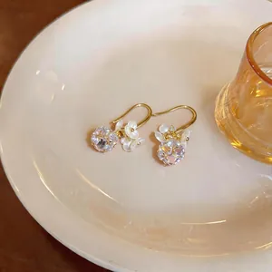 Close-up detail of elegant French style zircon flower earrings with gold hooks on a ceramic plate