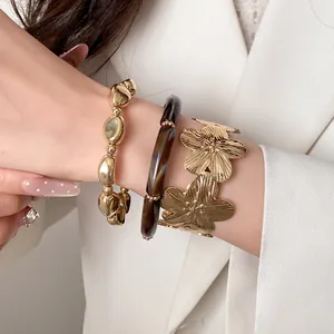 Detailed close-up of a stylish three-piece gold floral and brown resin bracelet set on a wrist