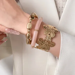 Close-up of three-piece bracelet set with gold flower cuff and pink resin beads on wrist