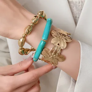 Detailed close-up of three-piece metal flower bangle and beaded bracelet set on wrist.