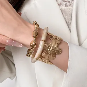Close-up detail view of a three-piece luxury gold metallic flower and marbled bead bracelet set