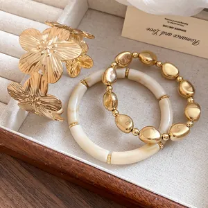 Detail of golden metal flower bangle and cream beaded bracelet set on velvet tray