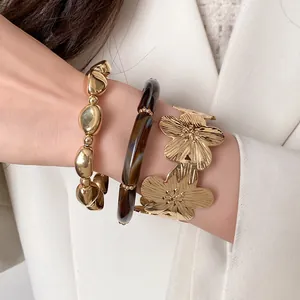 Detail view of 3-piece gold jewelry set featuring flower cuff and marbled resin bracelet