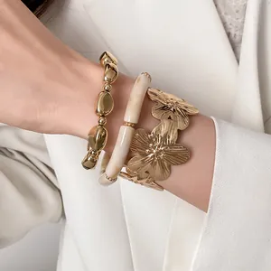 A detailed close-up of a 3-piece luxury gold floral and bead bracelet set on a model's wrist.
