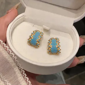 Close-up of vintage geometric gold earrings with turquoise stones in a white jewelry box.