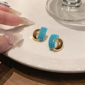 Close-up detail of vintage style gold C-shaped earrings with turquoise beads on a plate