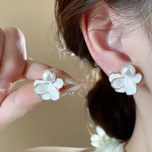 Close-up detail of white enamel flower earrings with central pearl and gold-plated edges