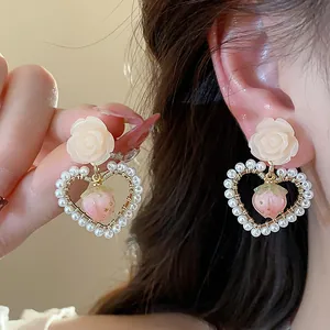 Detail of handmade flower and pearl heart earrings with pink strawberry charm
