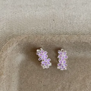 Primer plano de pendientes de aro plateados con pequeños dijes de flores moradas.