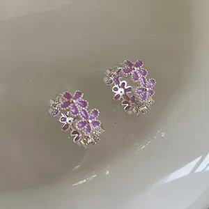 Detalle de pendientes de aro plateados con delicado esmalte de flores púrpuras