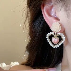 Close-up detail of sweet strawberry heart earrings with small pearls and a rose stud on ear