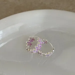 Primer plano de pendientes de aro plateados con flores moradas y brillantes circonitas
