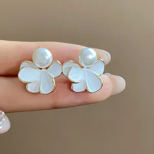 Detailed macro view of white enamel flower earrings with pearl and gold-plated edges