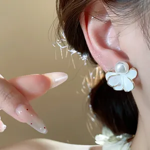 Close-up of elegant white enamel flower stud earring with a pearl center worn on ear