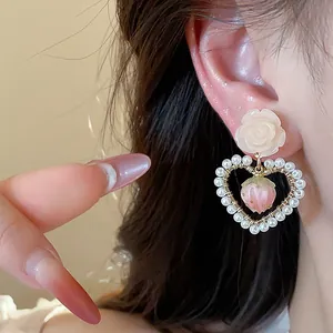 Close-up detail of floral pearl heart earrings featuring a sweet pink strawberry charm