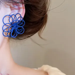 Close-up of blue spray-painted intertwined wire flower earrings worn by a model.