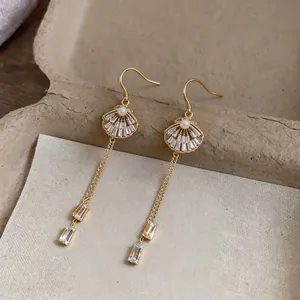 Detailed macro view of gold shell-shaped earrings with faux pearl and crystal tassel drops