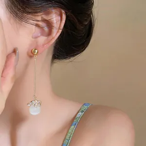 Detail view of long gold tassel drop earrings with white cat's eye bead worn by a model