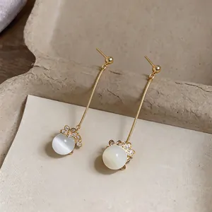 Close-up of elegant gold tassel earrings with white opal beads and floral details.