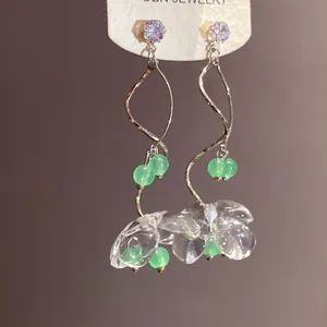 Détail rapproché de boucles d'oreilles fleurs en résine transparente et perles vertes