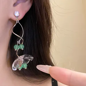 Gros plan détaillé de boucles d'oreilles muguet avec fleurs en résine et perles vertes.