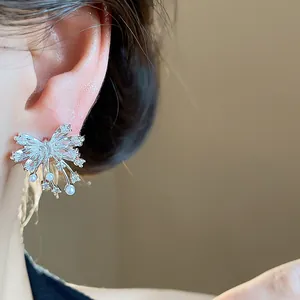 Detailed close-up of sparkling zircon butterfly stud earrings with small pearls on ear