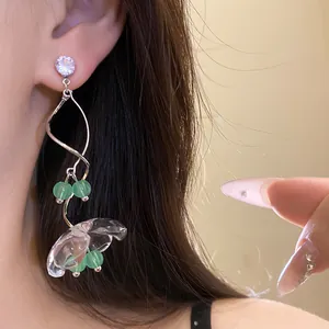 Gros plan de boucles d'oreilles fleur en résine transparente avec perles vertes sur modèle.