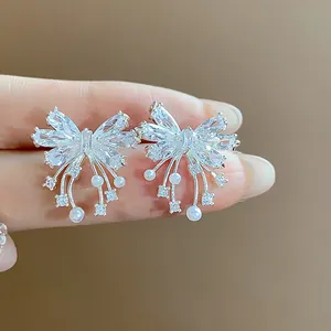 Close-up of elegant bow-shaped silver stud earrings with zirconia and pearls.