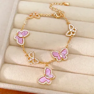 Exquisites Goldarmband mit rosa und klaren Zirkonia-Schmetterlingsanhängern auf Schmucktablett.
