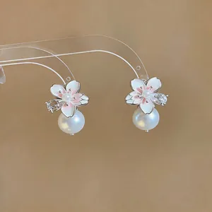 Close-up of enamel camellia flower earrings with zircon and dangling pearl details