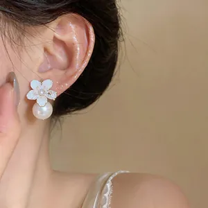 Close-up view of elegant camellia flower earrings featuring a large white pearl drop.