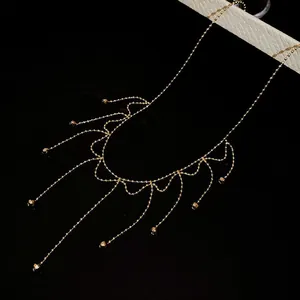 Detail view of a delicate gold-toned fringe necklace with tiny bead tassels on black.
