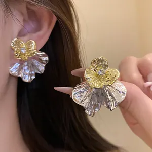 Dettaglio di eleganti orecchini a lobo a fiore oro e argento con strass centrale.