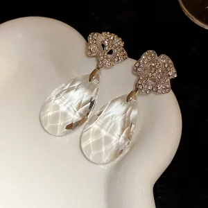Détail macro de boucles d'oreilles fleur argentées avec pendentifs gouttes cristallins.